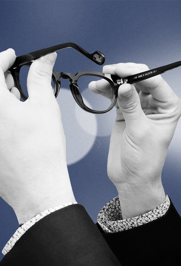 a pair of hands holding a black pair of eyeglasses